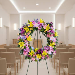 Colorful standing wreath with yellow lilies and pink mixed flowers on a metal easel in a chapel.