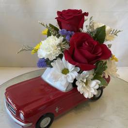 Red rose and daisy arrangement in a red toy car