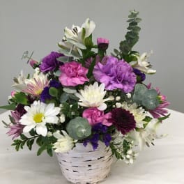 Mixed bouquet of white, pink, and purple flowers in a white basket