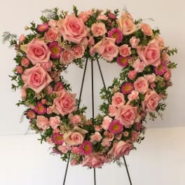 Heart-shaped floral wreath of pink roses and small pink blooms on a stand