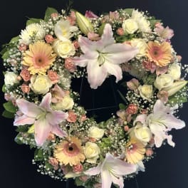 Heart-shaped floral wreath with pink lilies, cream roses, and peach gerberas