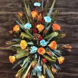 Tall floral spray with orange roses and blue accents on a stand