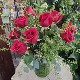 Arrangement of red roses with filler in a clear glass vase on a light wooden table