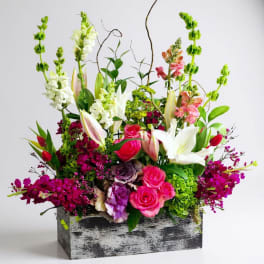 Mixed floral arrangement with pink roses, white lilies, and tall snapdragons in a rustic box