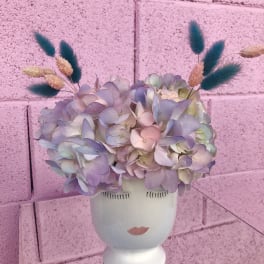 Pastel hydrangea arrangement in a white face vase with dried accents