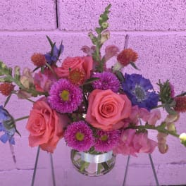 Pink roses and purple flowers in a clear glass vase