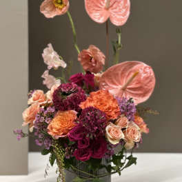 Pink and orange floral arrangement in a gray vase with tall anthuriums