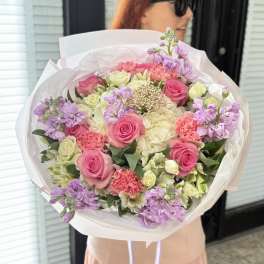 Large bouquet of pink and cream roses with lavender flowers in white wrap