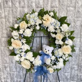 Heart-shaped floral wreath with cream roses, white flowers, and a blue ribbon on an easel