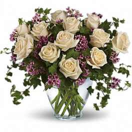 Cream roses and purple filler flowers in a clear glass vase