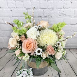 Pastel flower arrangement with roses, chrysanthemums, and daisies in a rustic container
