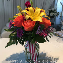 Bouquet of yellow lilies, orange roses, and purple flowers in a glass vase