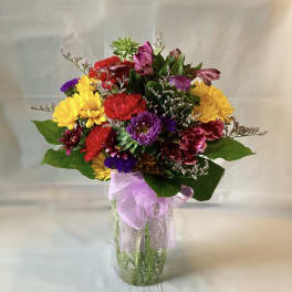 Colorful mixed bouquet in a clear glass vase with a lavender ribbon