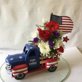 Floral arrangement in a patriotic truck-shaped container with an American flag topper