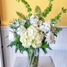 White floral arrangement in a clear glass vase with tall green spikes