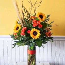 Sunflower and rose arrangement in a tall glass vase with a red ribbon