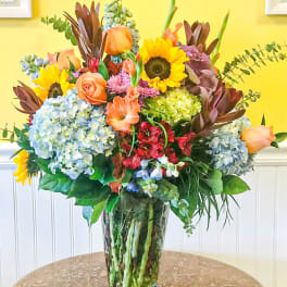 Mixed bouquet with sunflowers, roses, hydrangeas, and lilies in a glass vase