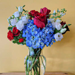 Red and white roses with blue hydrangeas in a glass vase
