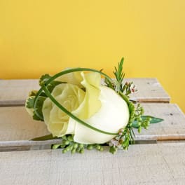 White rose boutonniere with small green accents on a wooden surface