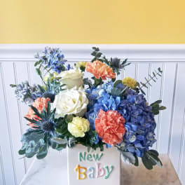 Colorful flower arrangement in a white vase labeled New Baby