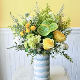 Yellow roses and white blooms in a tall striped vase