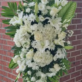 White funeral spray with lilies, roses, and daisies on an easel