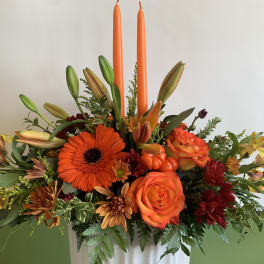 Orange and yellow floral arrangement with two tall orange candles