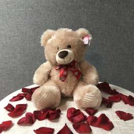 Teddy bear with a red ribbon sitting among rose petals