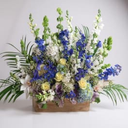 Tall floral arrangement with blue, white, and yellow blooms in a wooden box