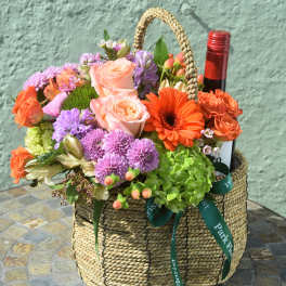 Woven basket of mixed colorful flowers with a wine bottle tucked among the blooms