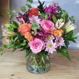 Mixed bouquet of pink, peach, and purple flowers in a glass vase