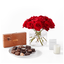Red roses in a glass vase with chocolates and a candle