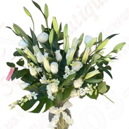 White roses and lilies in a glass vase with greenery