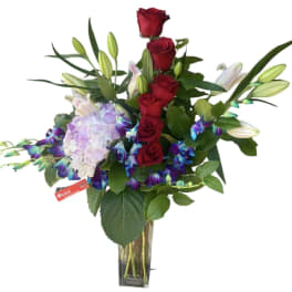 Red roses, lilies, and lavender hydrangea in a glass vase
