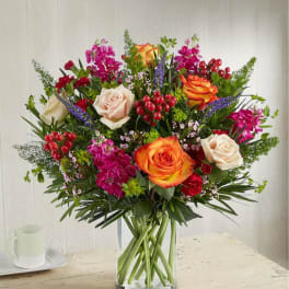 Mixed bouquet of roses and magenta flowers in a clear glass vase