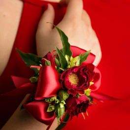 Red wrist corsage with small red flowers and satin ribbon on a wrist in a red dress