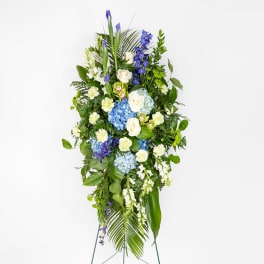 Tall standing spray of blue hydrangeas, white roses, and mixed blooms on a green easel
