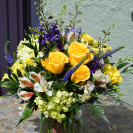 Yellow rose and purple flower arrangement with white blooms in a clear glass vase on a mosaic table