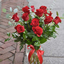 Arrangement of red roses with eucalyptus in a clear glass vase tied with a red ribbon.