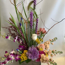 Tall mixed floral arrangement in a wooden box with purple orchids and peach blooms