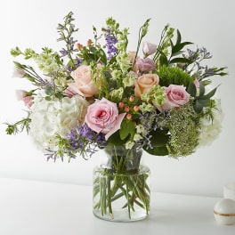 Mixed pastel bouquet of roses, hydrangeas, and purple flowers in a glass vase