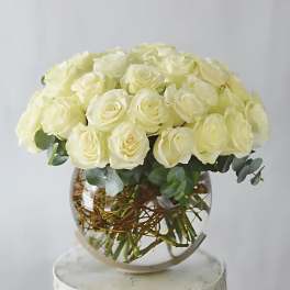 Round bouquet of cream roses in a clear glass vase