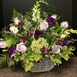 Basket arrangement of lavender roses, purple blooms, and white flowers