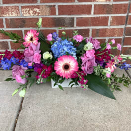 Colorful mixed flower arrangement with pink gerberas and roses in a white container