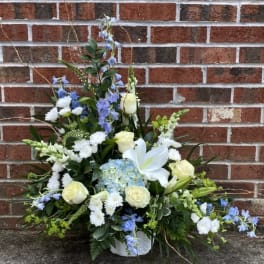 White and blue floral arrangement in a white basket against a brick wall