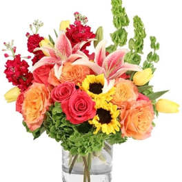Mixed bouquet of roses, lilies, sunflowers, and red blooms in a glass vase