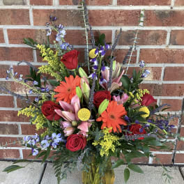 Mixed bouquet of red roses, lilies, and orange gerbera daisies in a glass vase