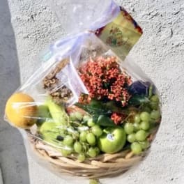 Fruit basket with grapes, apples, and flowers wrapped in clear plastic