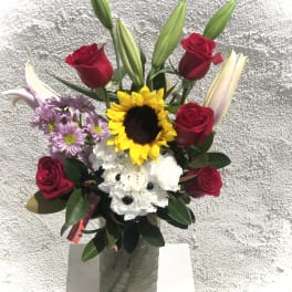 Bouquet of red roses, lilies, sunflowers, and white flowers in a vase