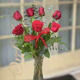 Red roses arranged in a clear glass vase with a red ribbon